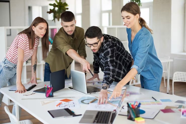 Designers gathered around a worktable, pointing at drawings and colour swatches together